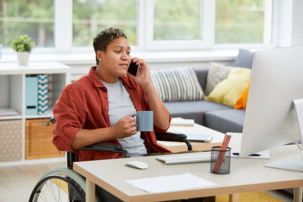 Disabled woman in wheelchair sitting at home desk on phone